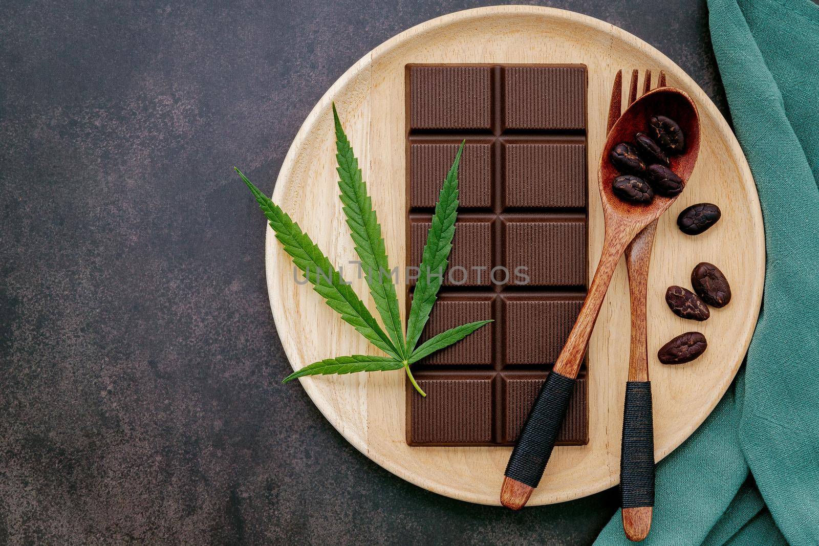 Food conceptual image of  cannabis leaf  with dark chocolate and fork on dark concrete background. by kerdkanno