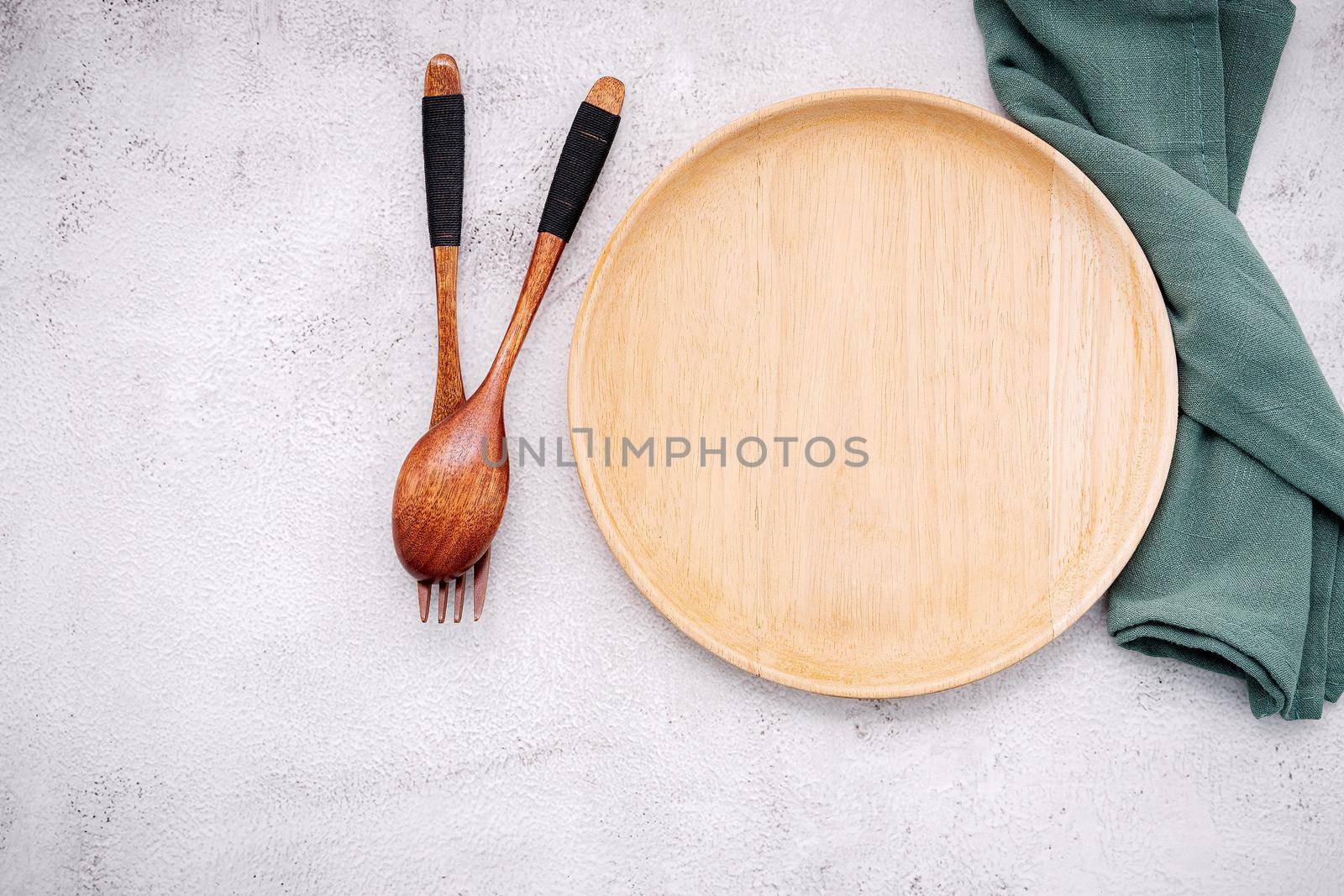 Food conceptual image of wooden plate with spoon and fork on white concrete background.