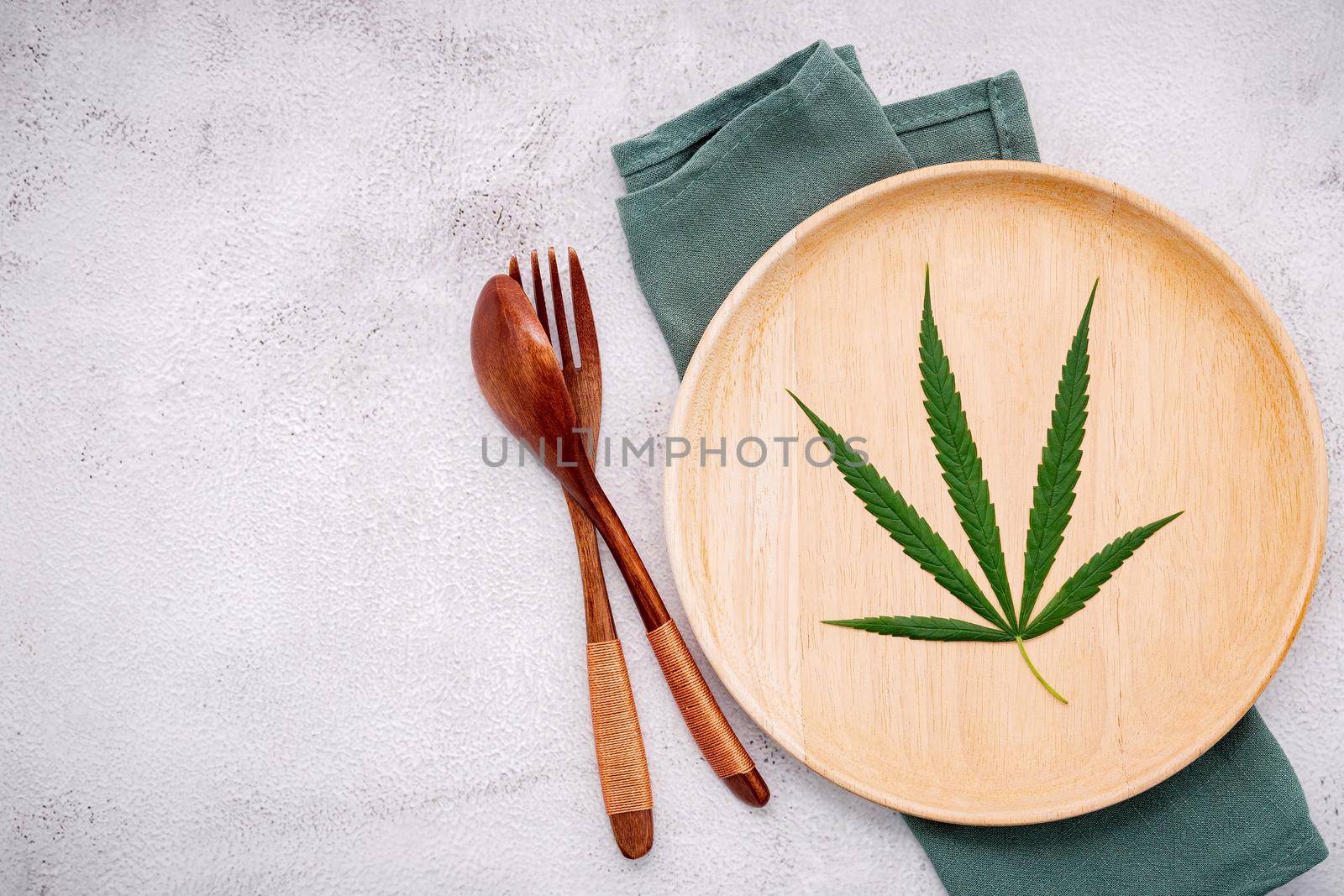 Food conceptual image of a cannabis leaf  with spoon and fork on white concrete background. by kerdkanno
