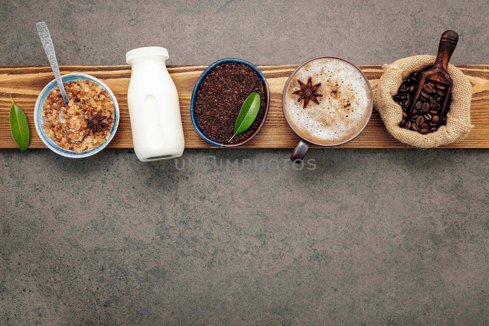 Roasted coffee beans with coffee powder and flavourful ingredients for make tasty coffee setup on dark stone background.