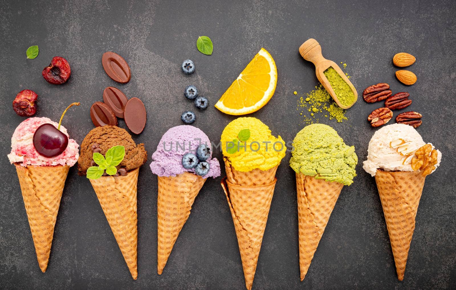 Various of ice cream flavor in cones blueberry ,green tea ,pistachio ,almond ,orange and cherry setup on dark stone background . Summer and Sweet menu concept.  by kerdkanno