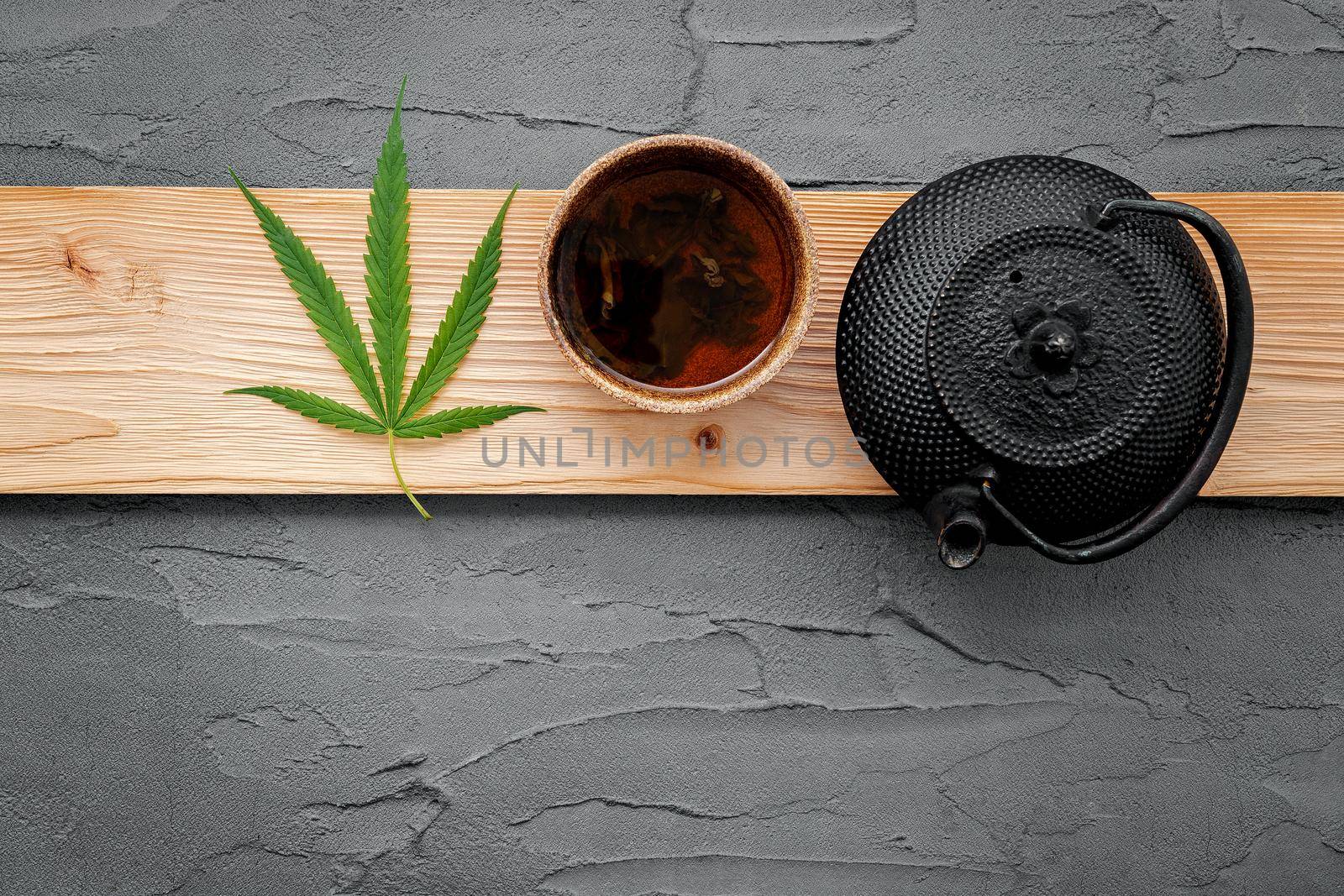 Vintage teapot with cannabis herbal tea and fresh marijuana leaves set up on concrete background.