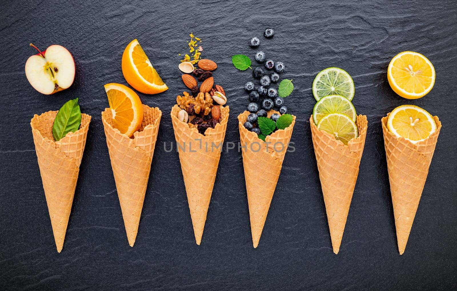 Various of ingredient for ice cream flavor in cones blueberry ,lime ,pistachio ,almond ,orange ,chocolate ,vanilla and coffee set up on dark stone background . Summer and Sweet menu concept.