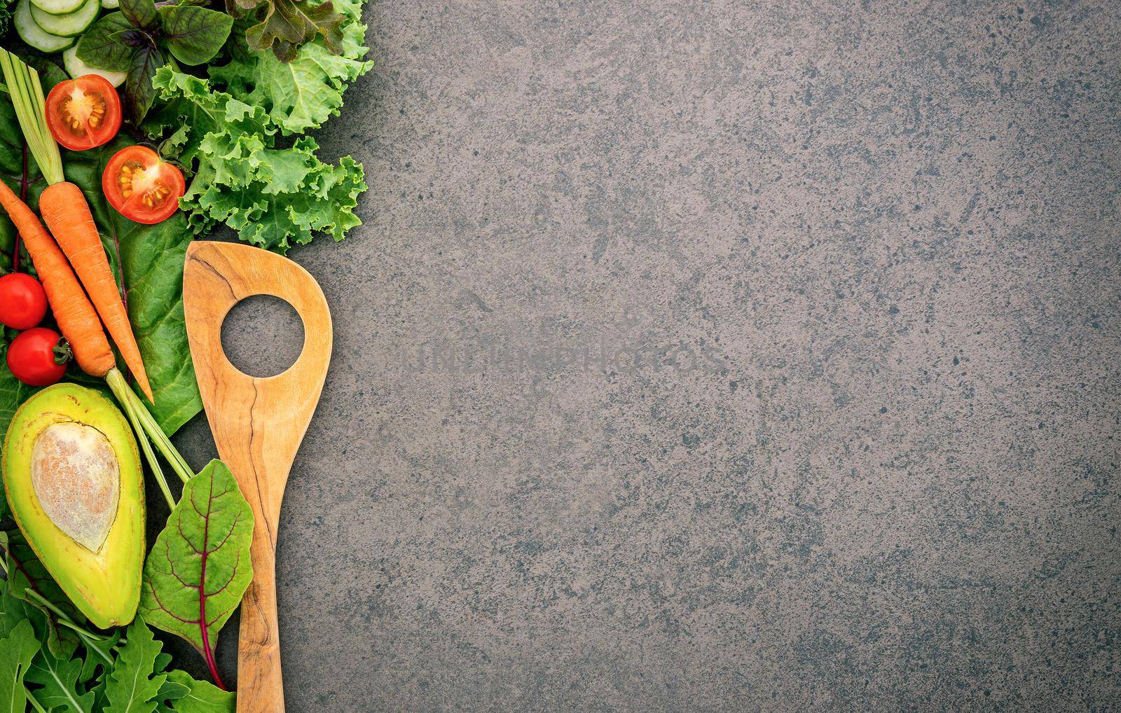 Healthy food and cooking concept wooden spatula and vegetables on dark stone background.