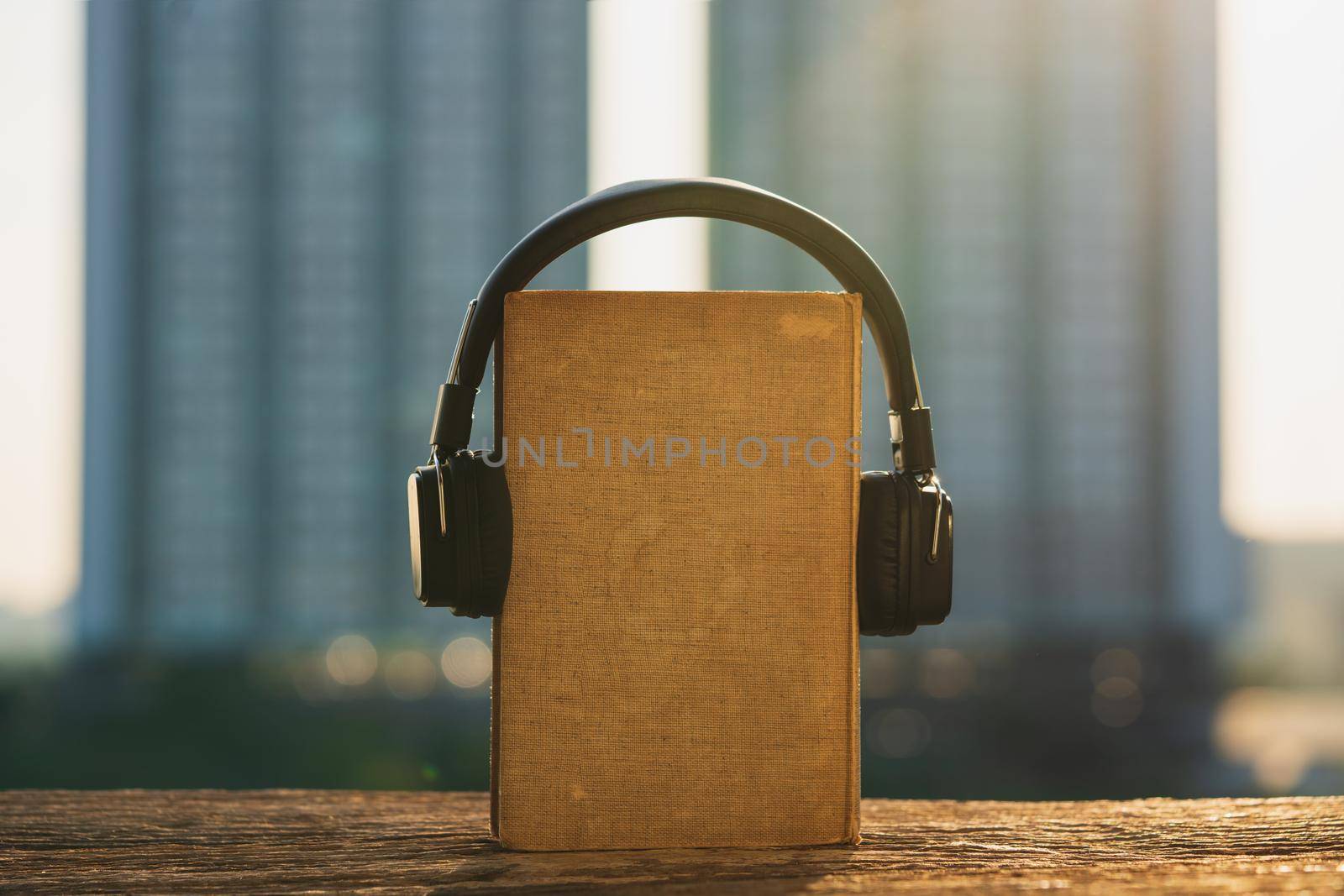 Audio book concept. Headphones and old book on wood with city background