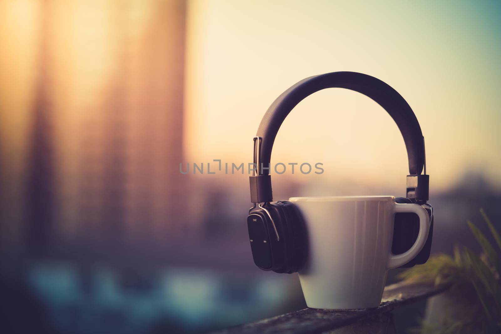 Headphones and coffee cup on blurred city background. Music concept. View of sunrise time, Vintage tone filter