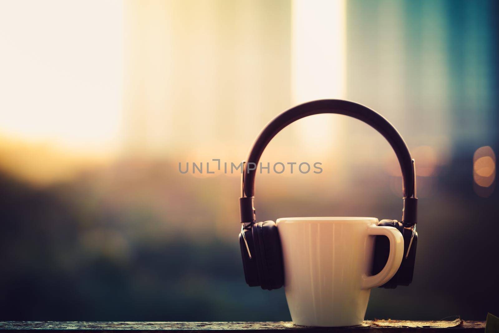 Headphones and coffee cup on blurred city background. Music concept. View of sunrise time, Vintage tone filter