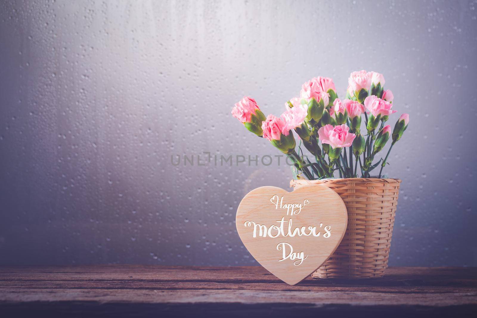 Still life with sweet carnation flowers in basket on wooden table, Mothers day concept With a message for Happy Mother's Day on a wooden heart