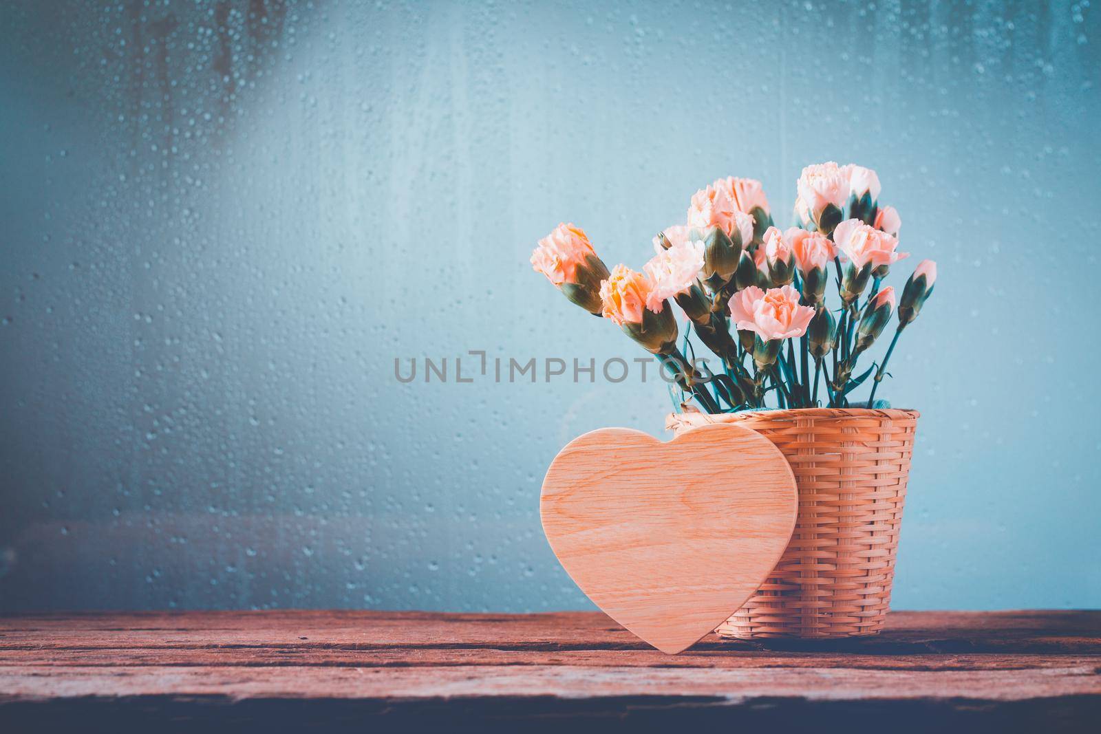 Still life with sweet carnation flowers in basket on wooden table,Heart wooden empty for Happy Mother's Day and Valentines Day concept