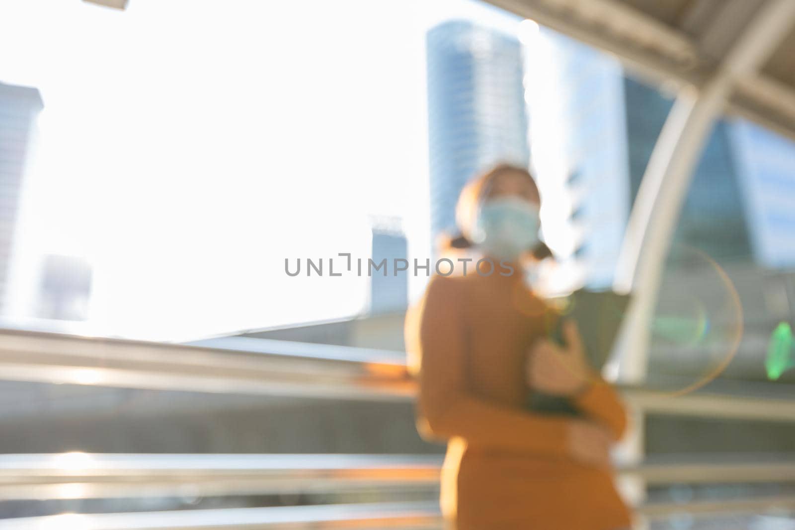 Blurred woman wearing a mask to the sunny city of the morning, Abstract background