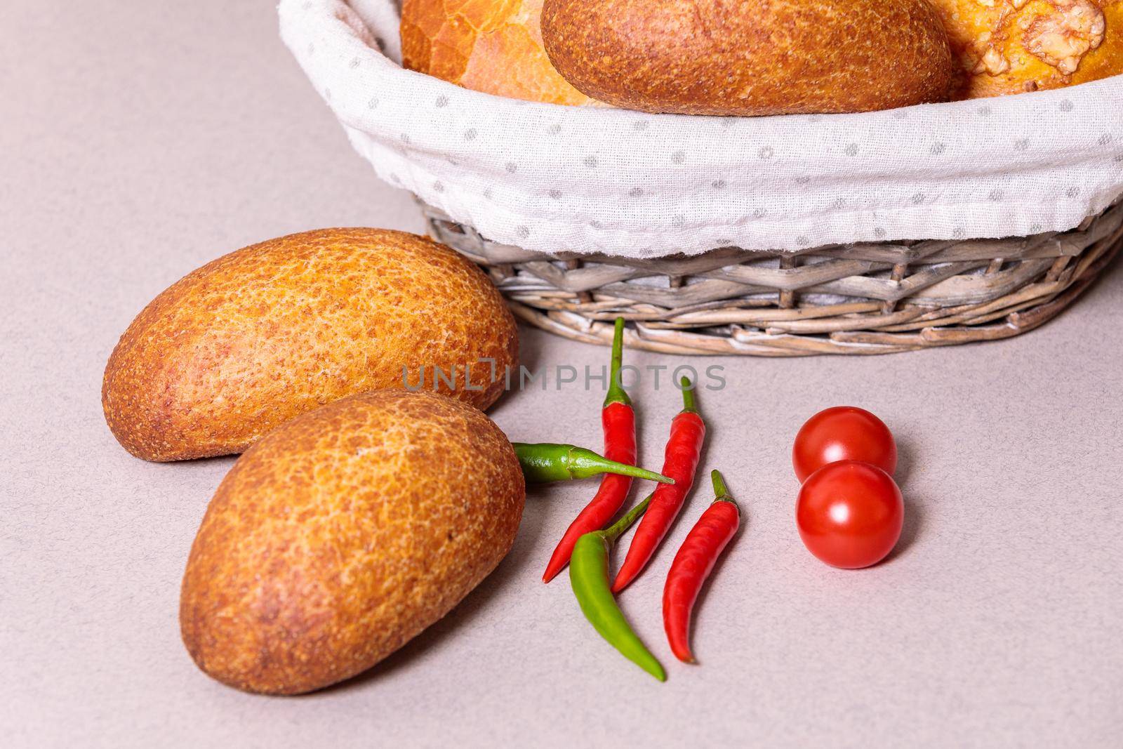 Fresh bread in a basket on the table with red peppers and tomatoes. by Yurich32