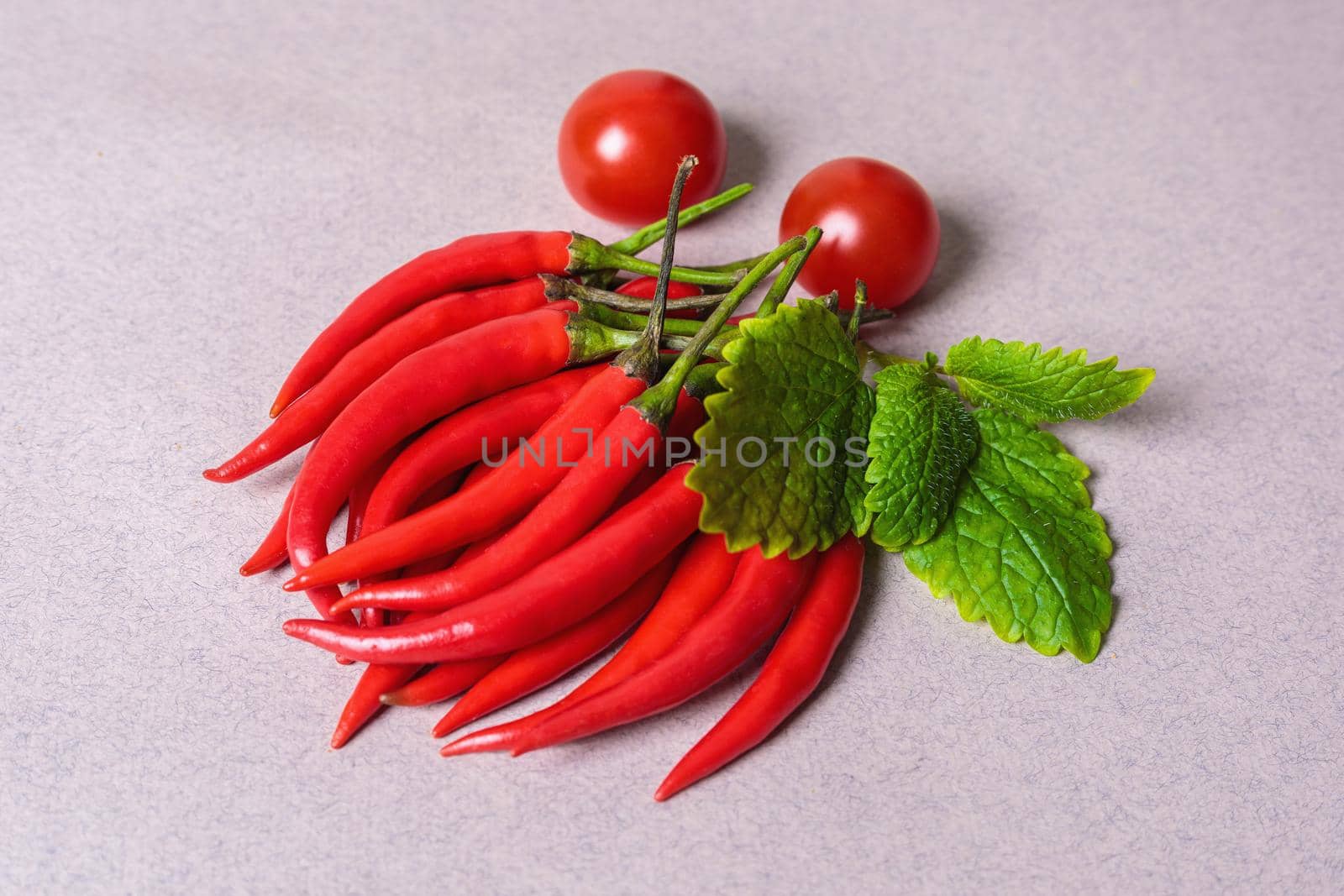 Slide of red chili peppers with one red tomato on a light background. View from above.