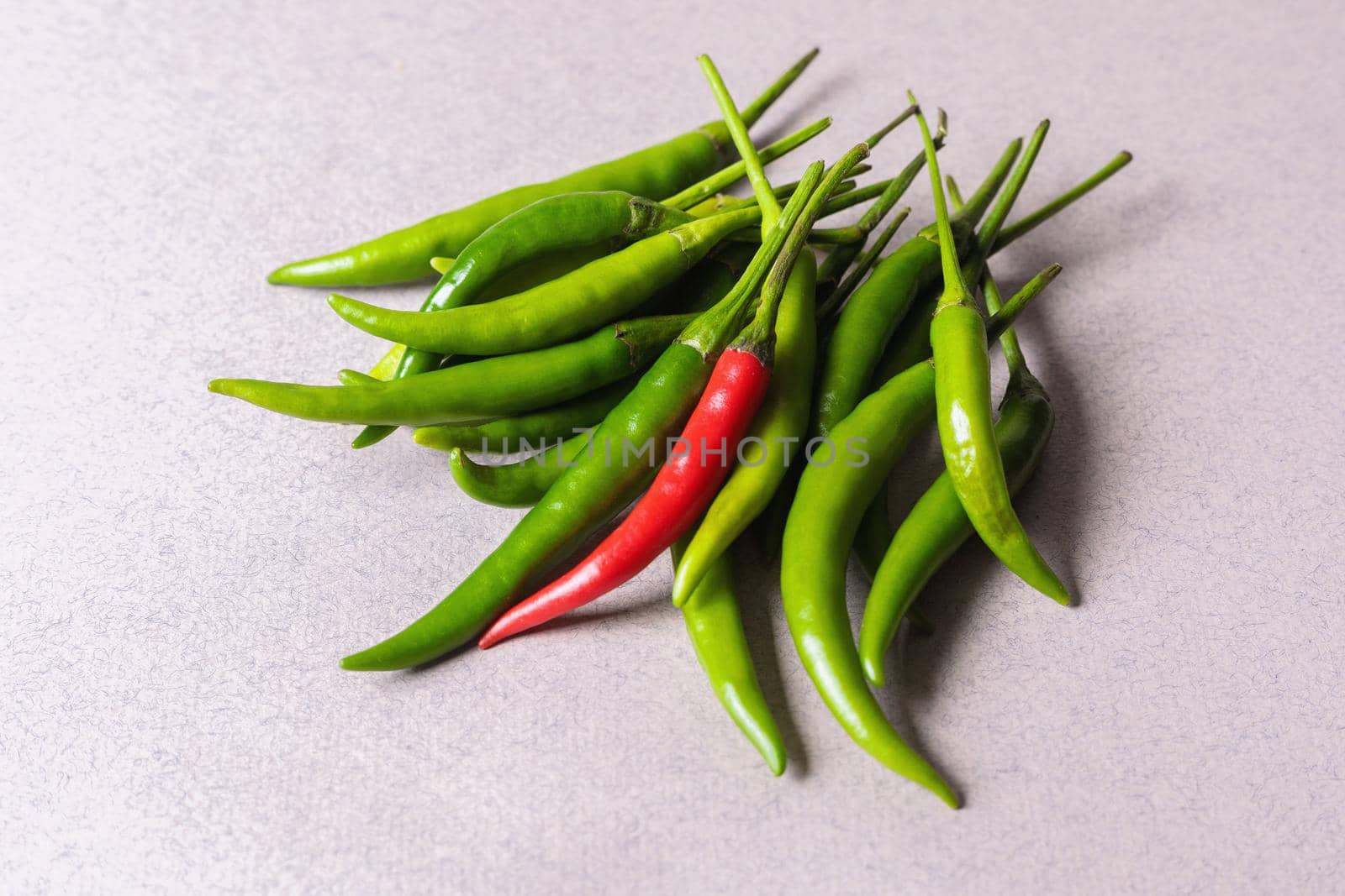 Slide of green chili peppers with one red on a light background. View from above.
