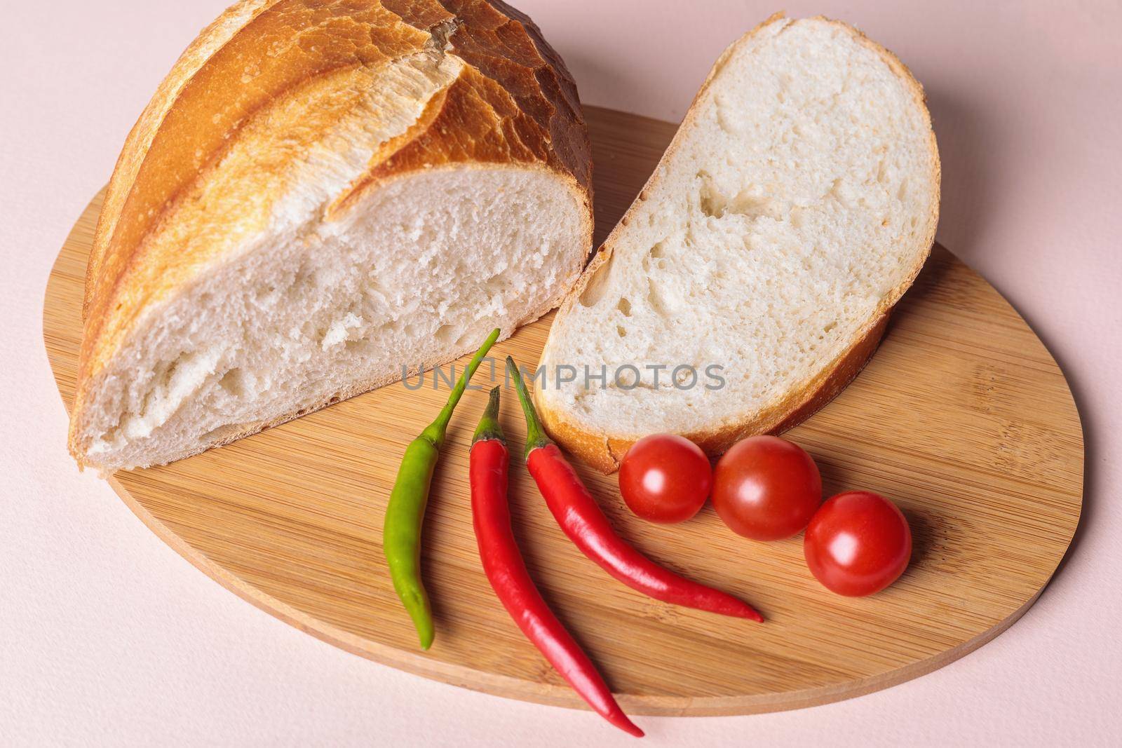 Sliced pieces of white bread with red peppers and tomatoes on a cutting board. Light background