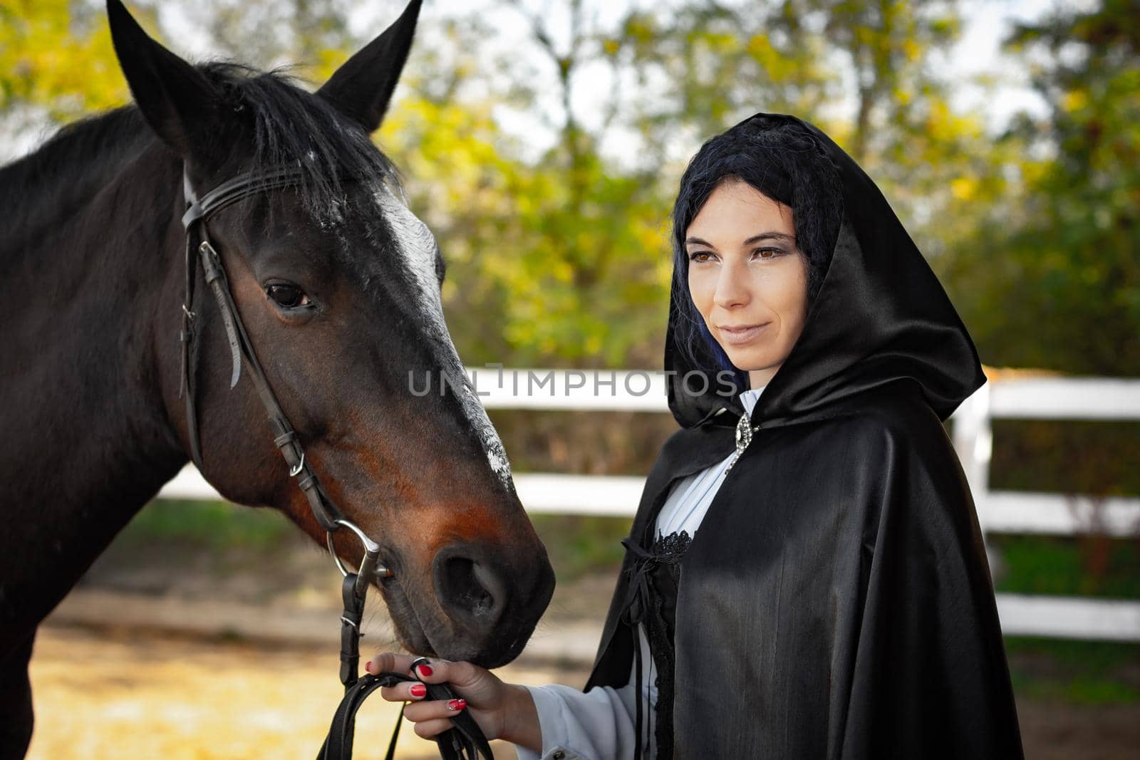 Portrait of a beautiful girl dressed in medieval style, the girl holds a horse by the bridle