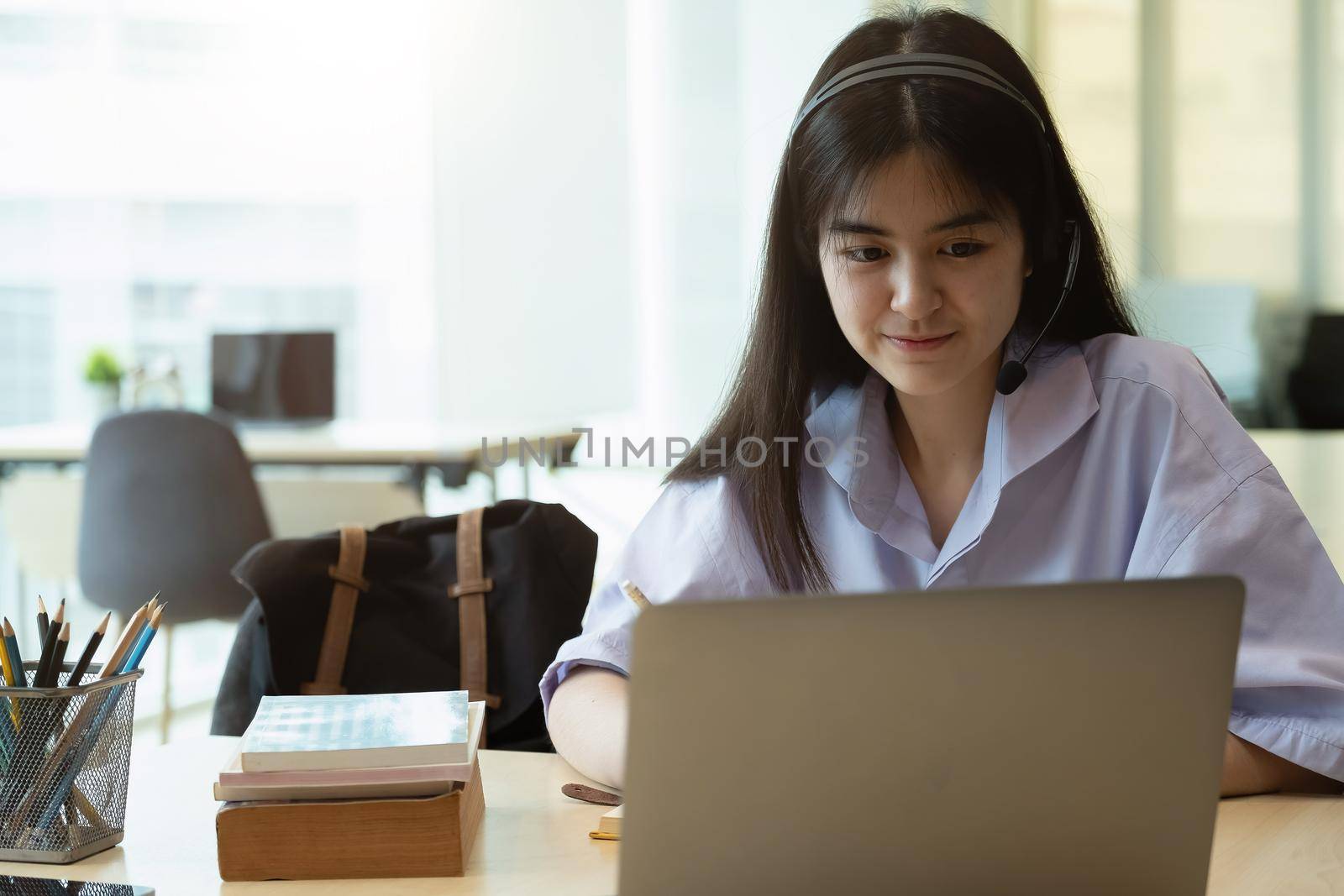 Portrait of a beautiful asian young woman studying while sitting at the table with laptop computer and notebook at home - elearning concept. by nateemee