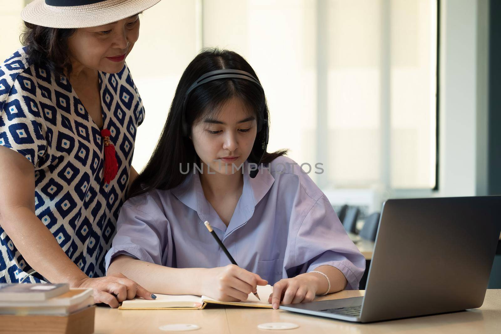 Asian mother with computer notebook teaching daughter to learn or study online at home, Homeschooling online concept. by nateemee