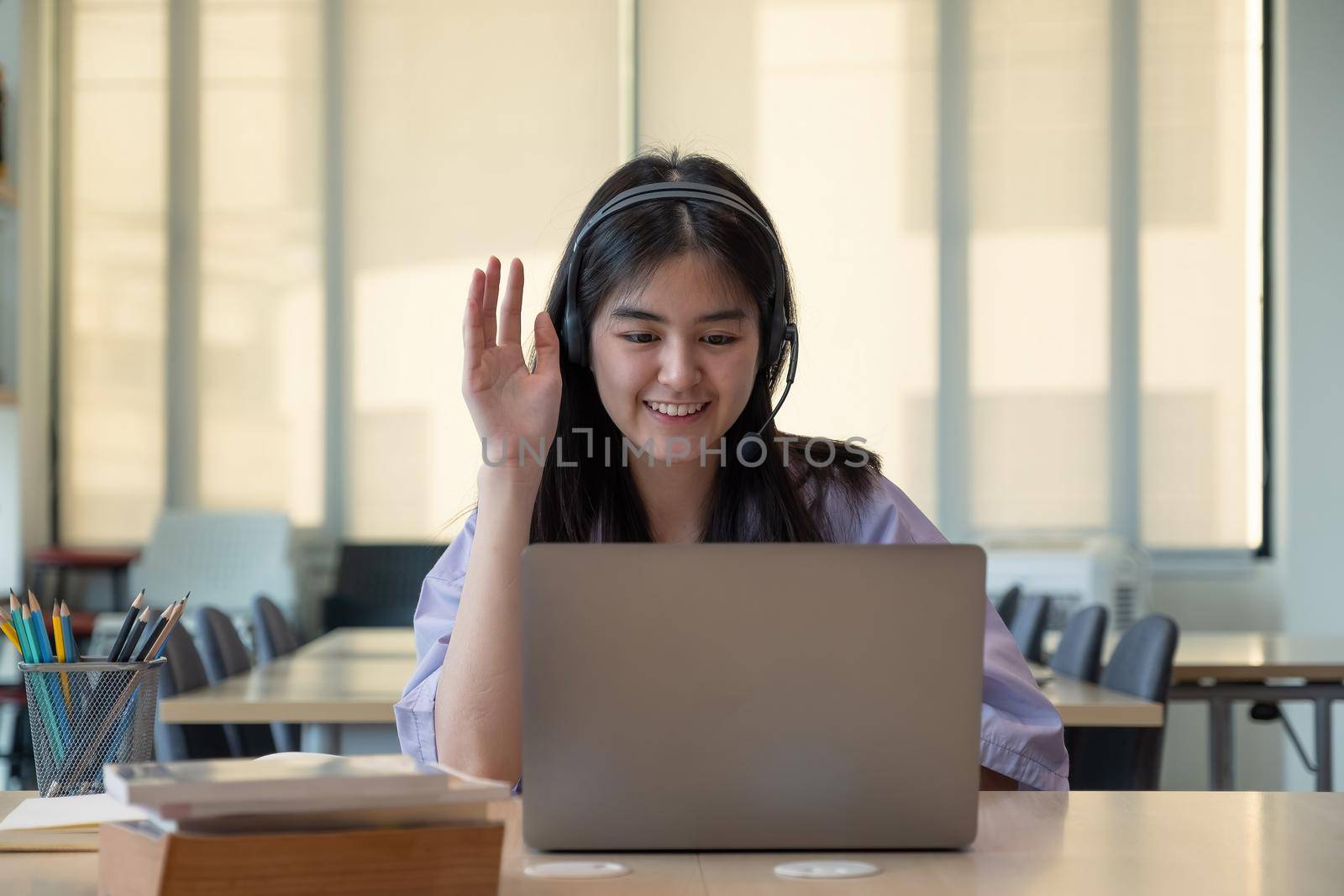 Smiling Asian girl in headphones have video call distant class with teacher using laptop, happy small child wave greeting with tutor, study online on computer, homeschooling concept. by nateemee