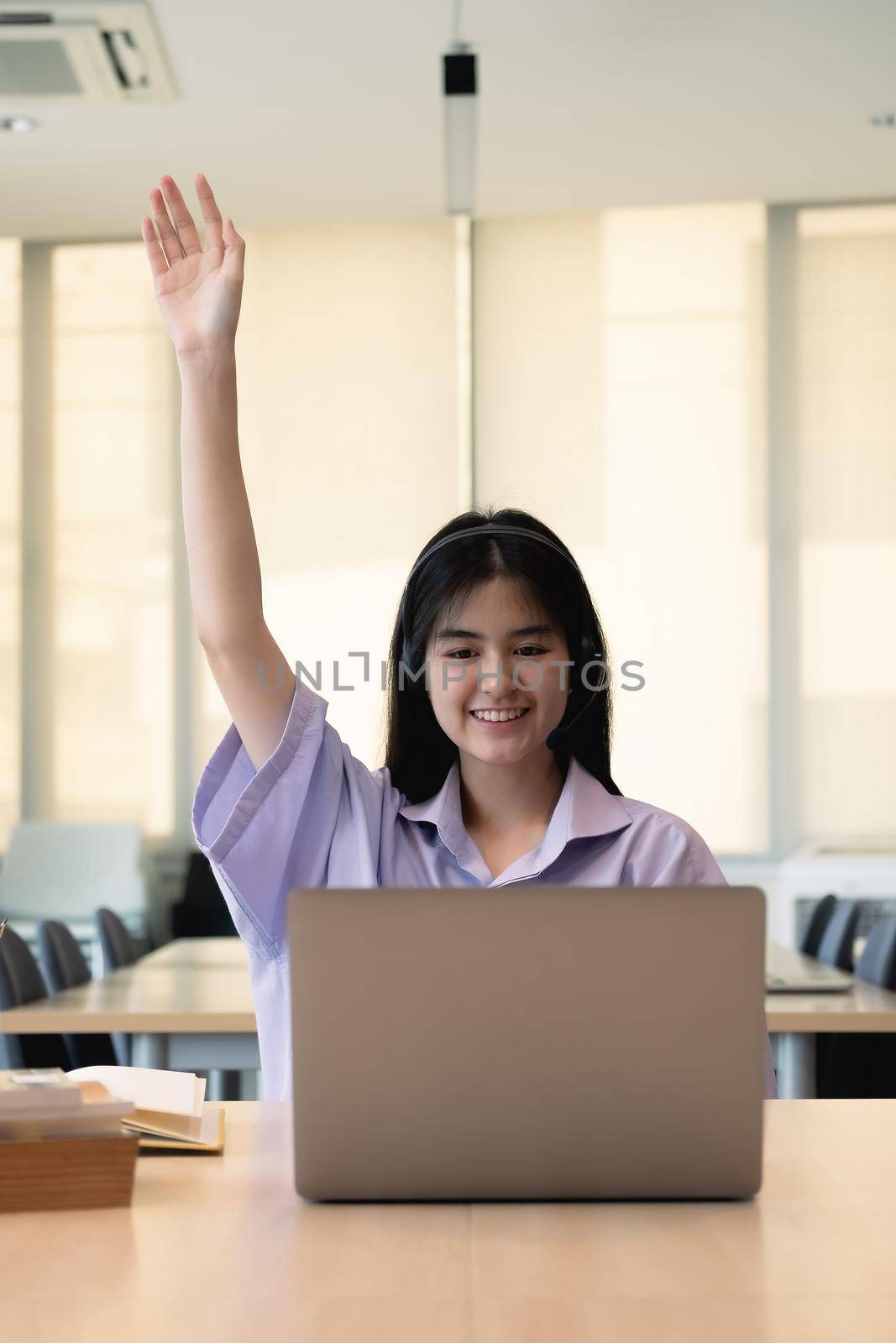 Smiling Asian girl in headphones have video call distant class with teacher using laptop, happy small child wave greeting with tutor, study online on computer, homeschooling concept. by nateemee