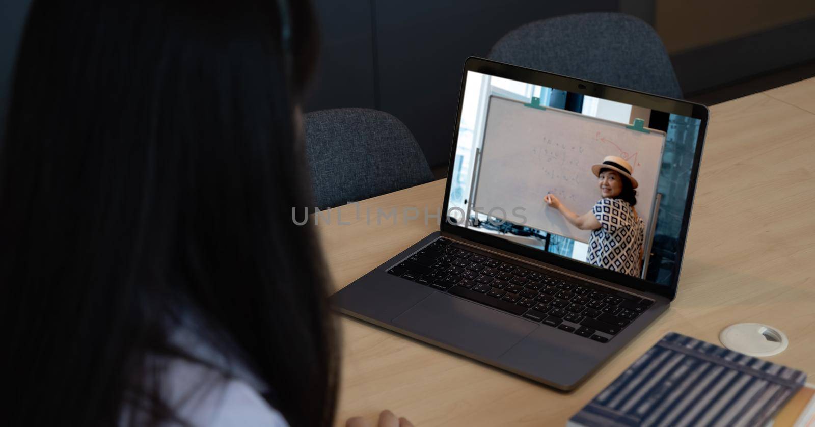 Asian young girl student learning virtual internet online class from school teacher by remote meeting due to covid pandemic. Female teaching by using headphone and whiteboard by nateemee