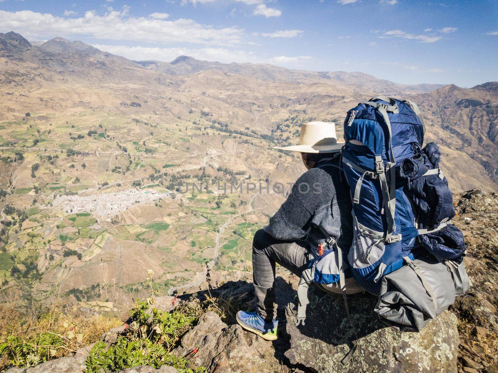 Traveler man with hat and backpack sitting on a rock watching the landscape, Travel lifestyle
