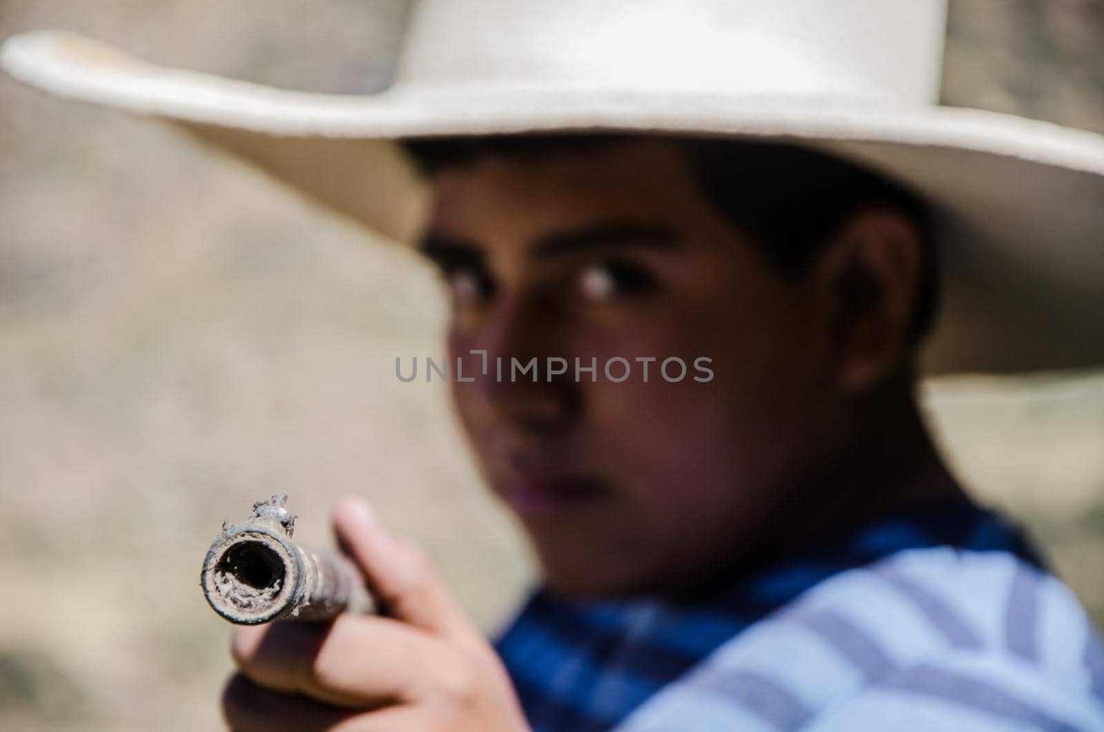 Close up face of boy with hat pointing with a rifle