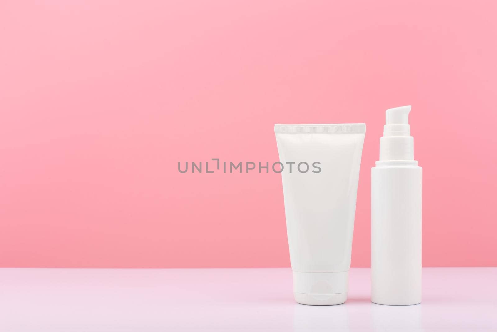 Two white cosmetic tubes on white table against pink background with copy space.Face cream, lotion or balm concept by Senorina_Irina