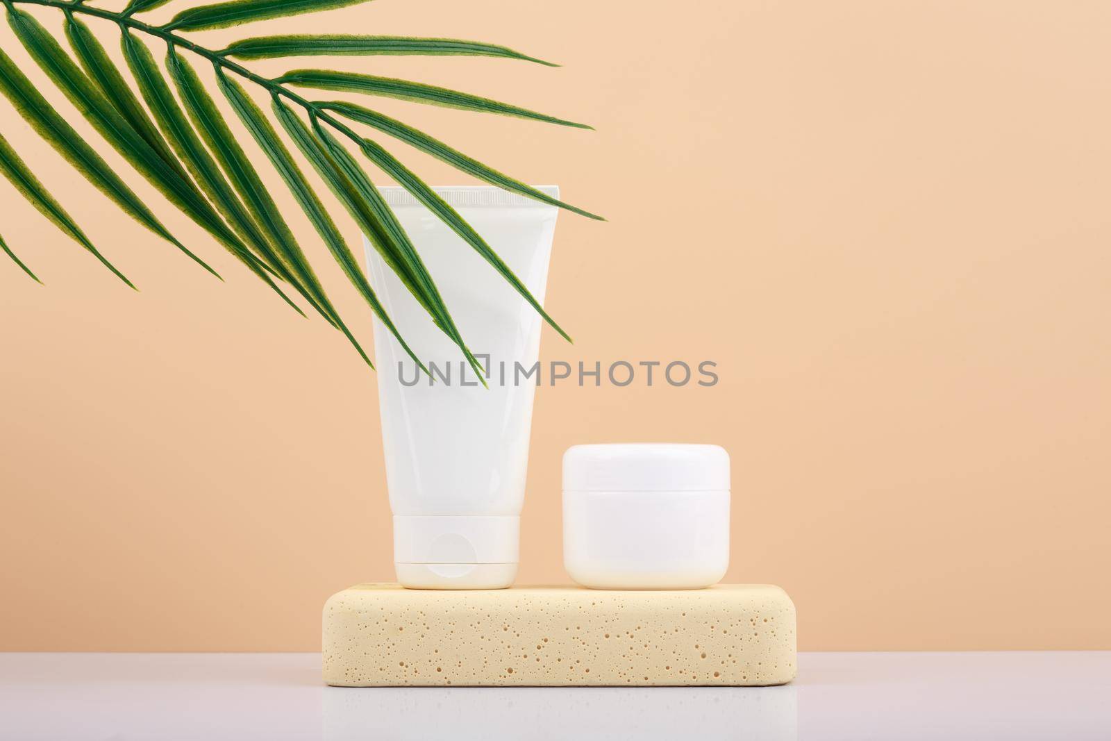 Hand cream and cuticle oil on stone podium against beige background with palm leaf and copy space by Senorina_Irina