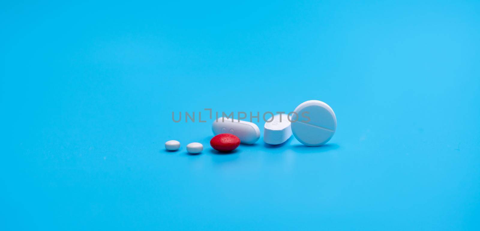 Group of round and oval white tablets pills, red sugar-coated tablets pills on blue background. Pharmacy shop and pharmacy department banner. Pharmaceutical industry. Health care. Drugs in daily life. by Fahroni