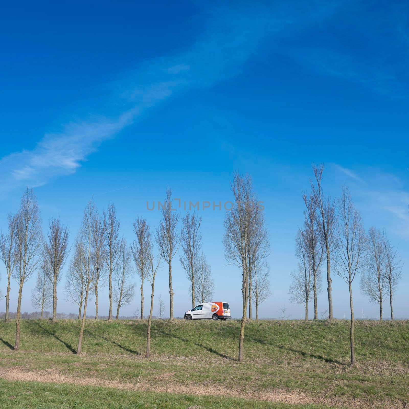 car of mail delivery on dyke of goeree overflkakkee in the netherlands under blue sky by ahavelaar