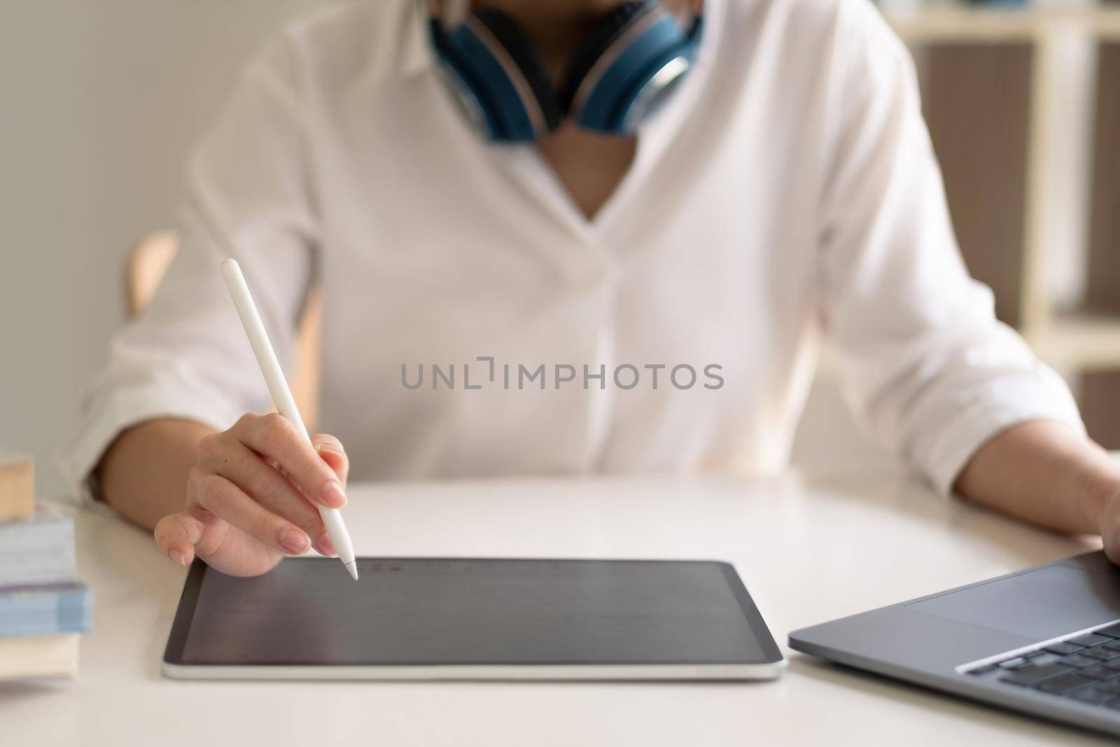 Close up of female worker working from home with digital tablet, laptop and headphone in home office room. by nateemee