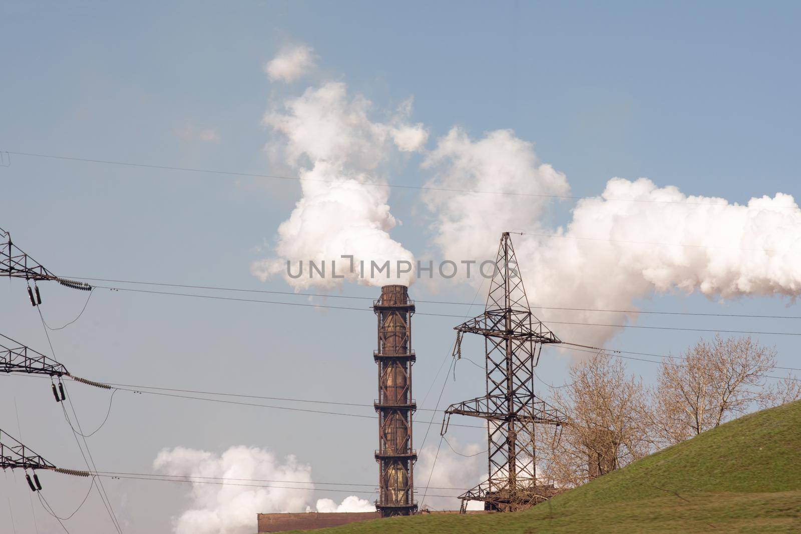 Smoke from the pipe of an industrial enterprise. Tower of a high-voltage power line. On a bright sunny day.