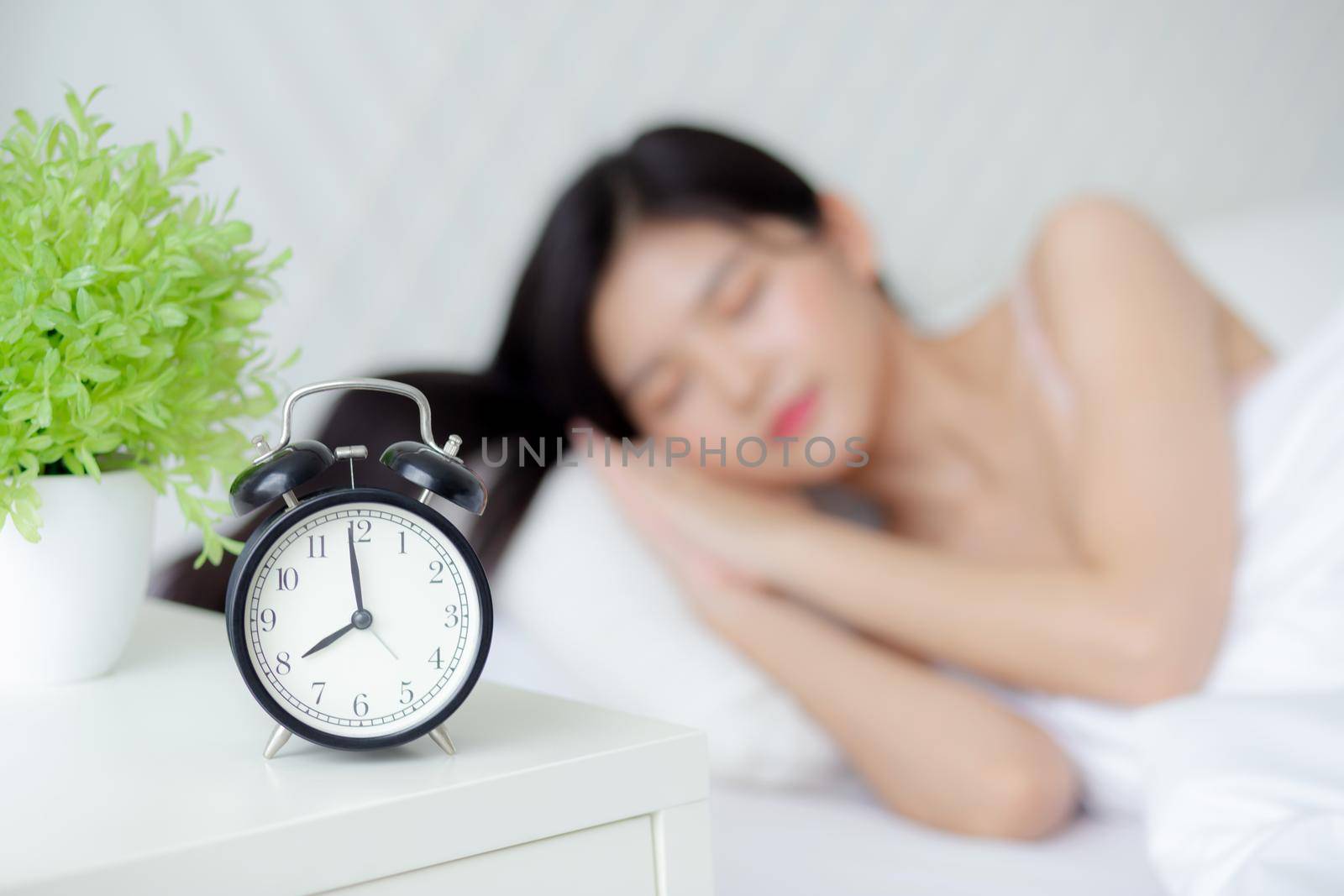 beautiful young asian woman sleep with relax on the bed with alarm clock in the morning, girl sleep with cozy and comfort after tired in the bedchamber, oversleep with time late, lifestyle concept.