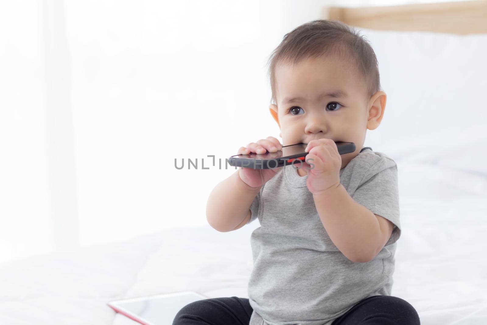 Portrait of cute little baby girl sitting with cozy on bed at bedroom, happiness of toddler, newborn 6-11 months with innocence and expression with cheerful, child charm, indoors, one person.