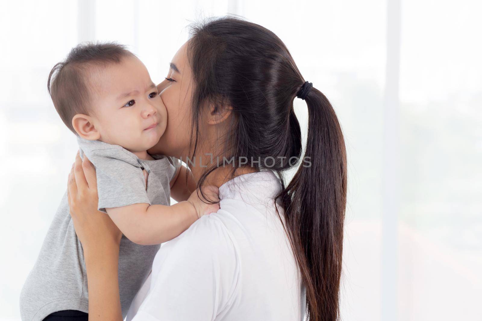 Young asian mother holding little baby girl together in the bedroom at home, mom carry child and care, woman and kid with carefree, toddler and parent, emotion and expression, family concept. by nnudoo