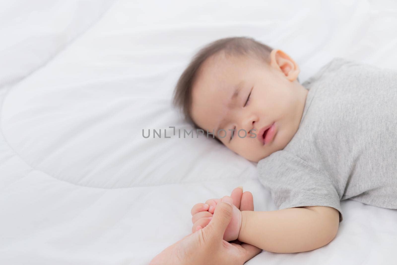 Young asian mother touch hand of little baby girl with tender on bed in the bedroom, mom love newborn and care, woman with expression with child together, parent and daughter, family concept.