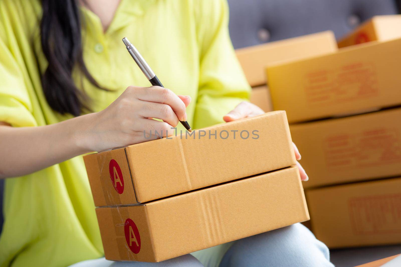 Closeup hand of young asian woman writing address on parcel box at home for delivery order to customer, shipping and logistic, merchant online and seller, business owner or SME, online shopping.