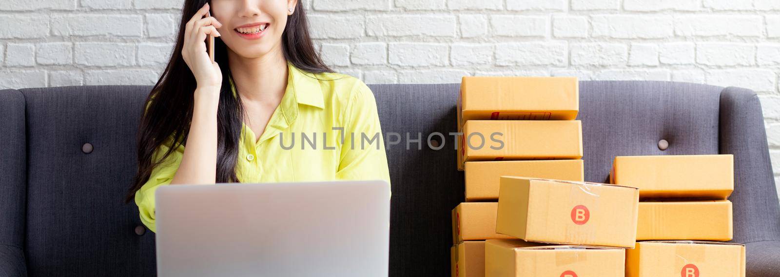 Young asian woman is entrepreneur talking with customer and using laptop computer while order purchase online at home, logistic and delivery, online shopping, female is seller of business SME.