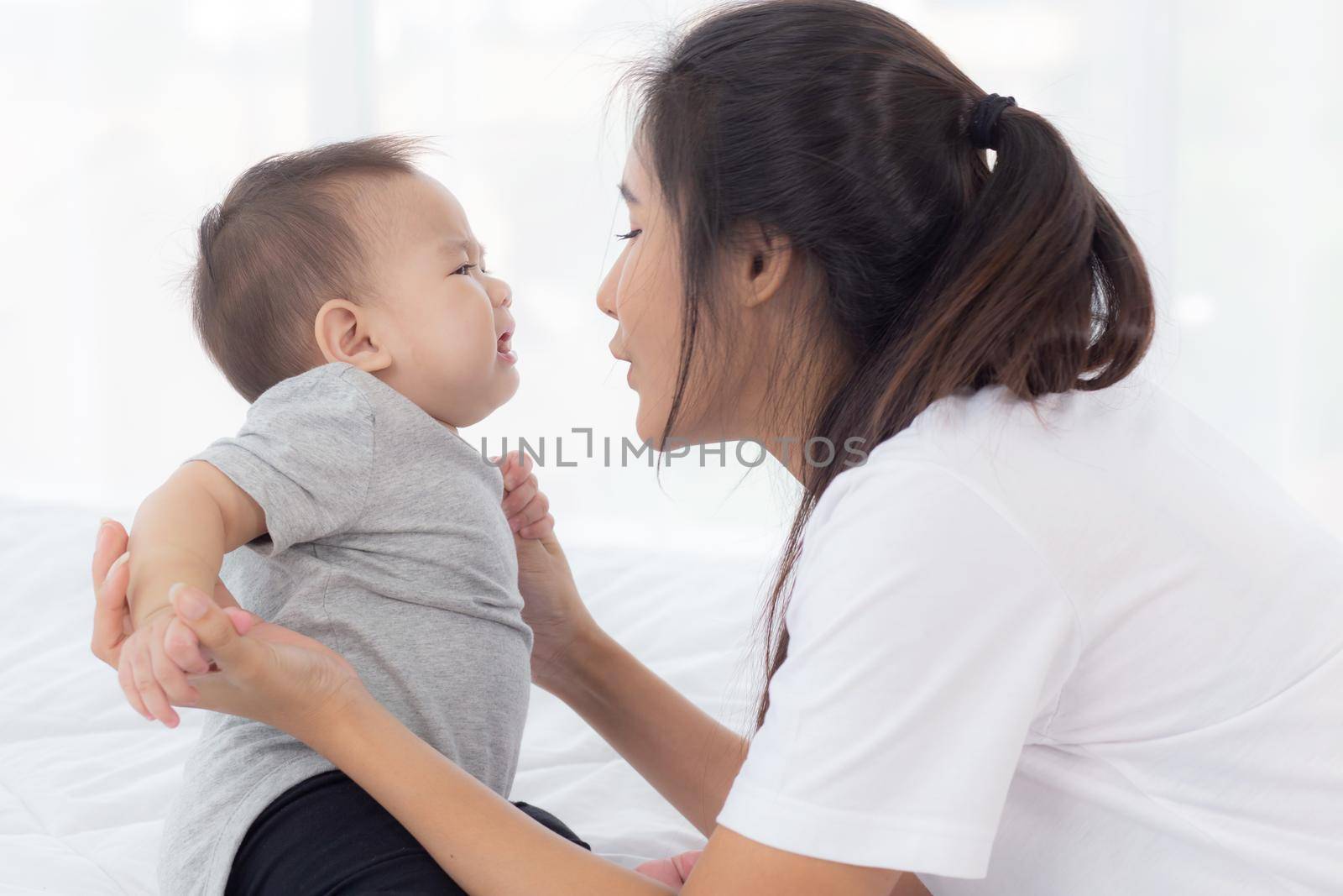 Young asian mother holding little baby girl together in the bedroom at home, mom carry child and care, woman and kid with carefree, toddler and parent, emotion and expression, family concept. by nnudoo