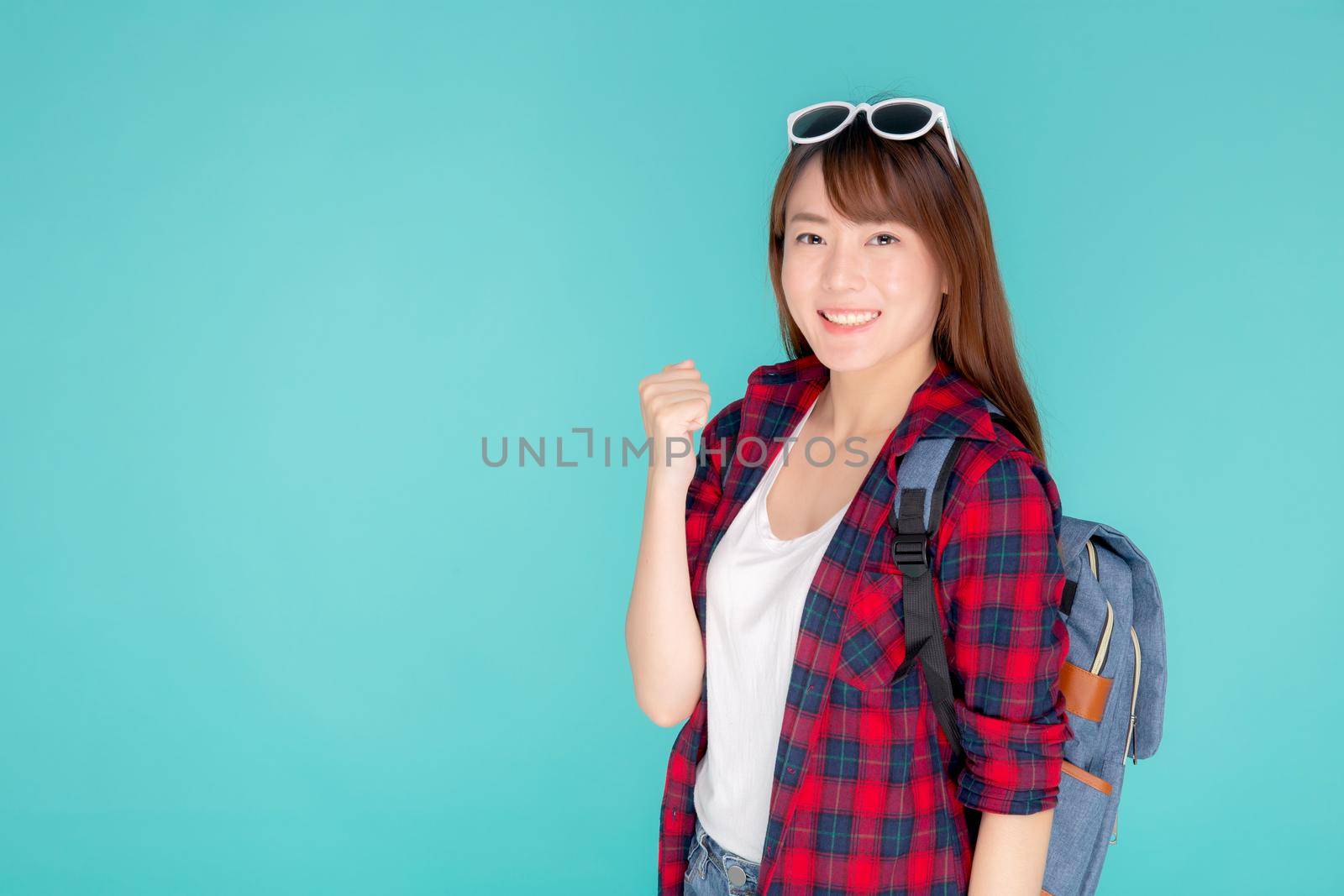 Beautiful portrait young asian woman wear sunglasses on head smile confident and excited summer holiday isolated blue background, model girl fashion having backpack, travel concept.