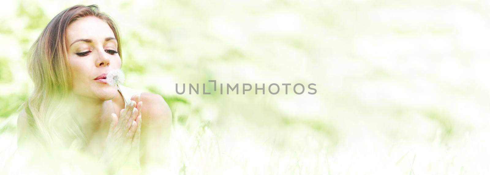 Beautiful young woman blowing dandelion lying on grass