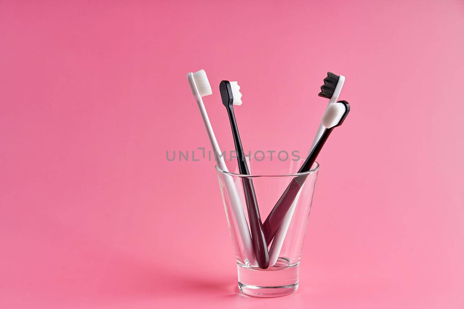 Fashionable toothbrush with soft bristles. Popular toothbrushes. Hygiene trends. Kit of toothbrushes in glass on pink background.