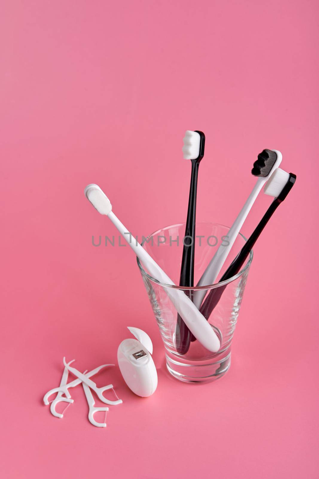 Fashionable toothbrush with soft bristles. Popular toothbrushes. Hygiene trends. Oral hygiene kit. Toothbrushes in glass, floss thread and toothpicks on a pink background.