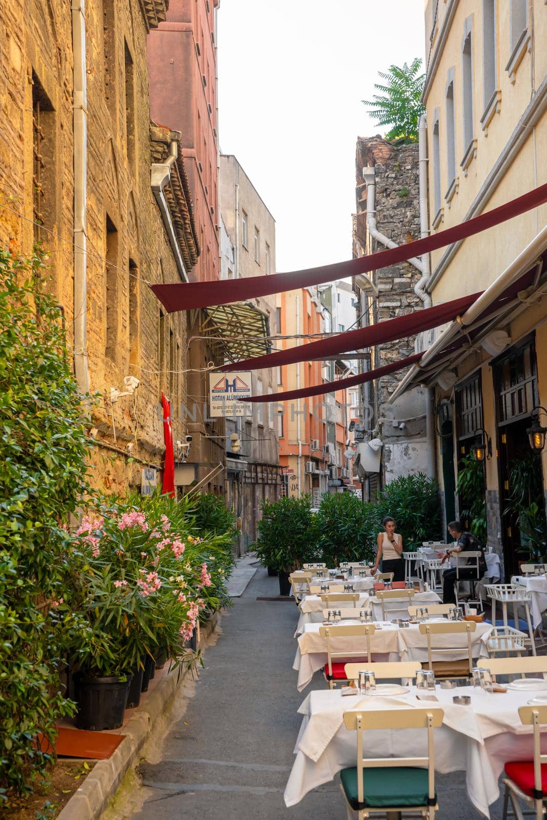 A narrow street half lined with restaurant tables. Summer area of the restaurant on a narrow street. Turkey , Istanbul - 21.07.2020