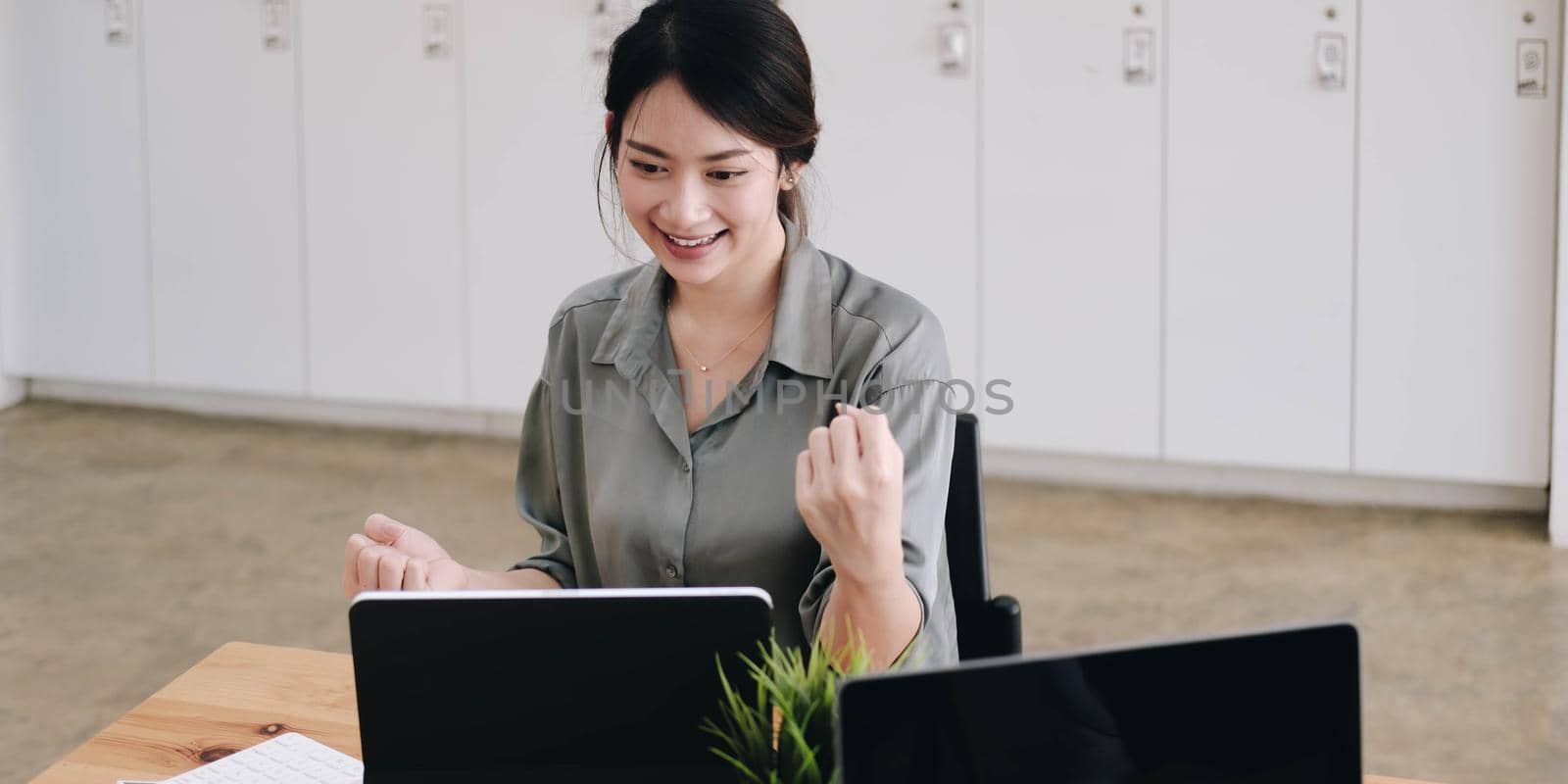 Portrait of happy young successful businesswoman celebrate something with arms up. Happy woman sit at office and look at laptop.