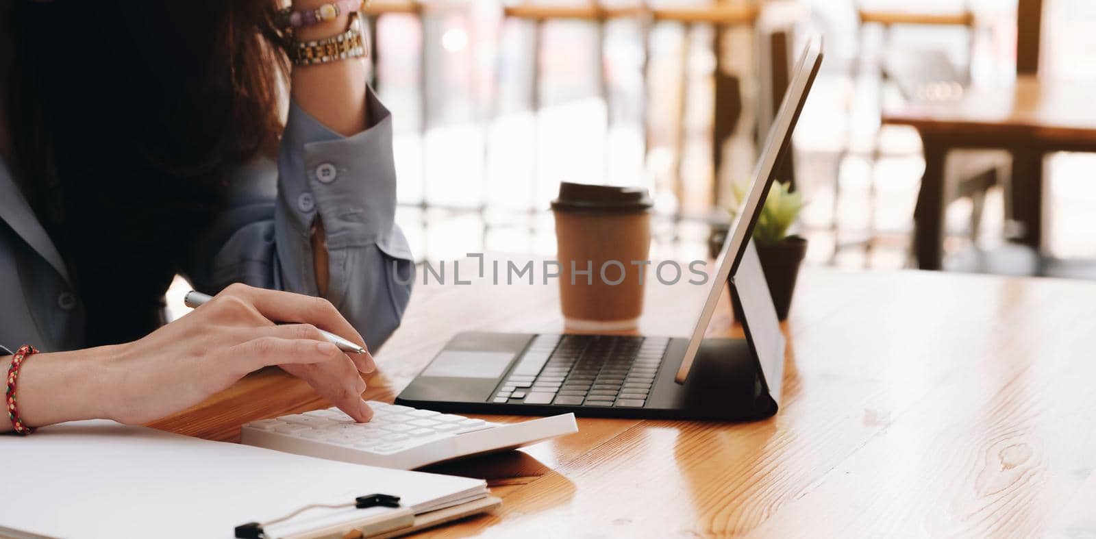 Asian woman pressing calculate for prepare information of report to correct. Still holding a paper work of laptop by wichayada
