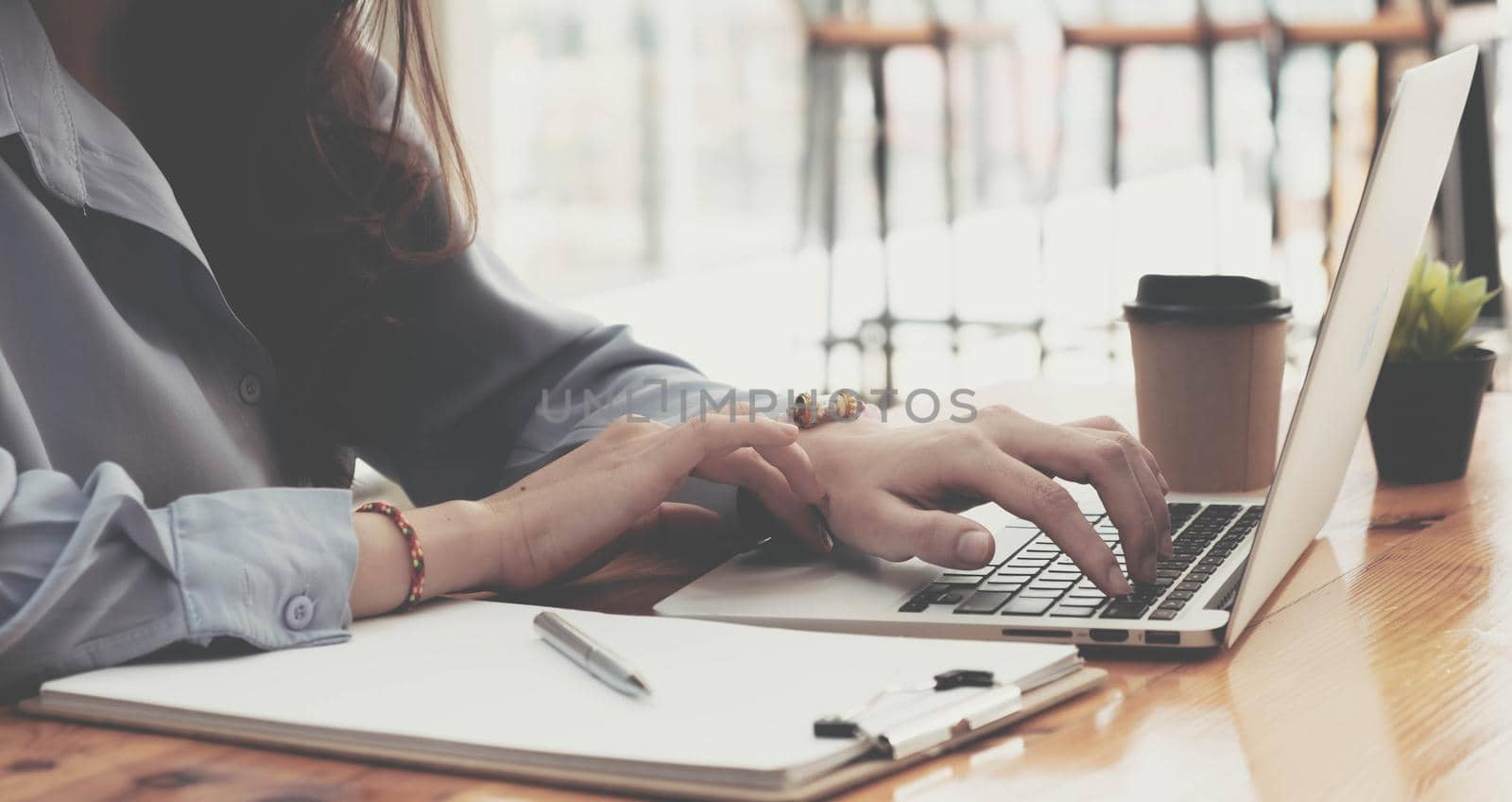 Typing on laptop keyboard. Close-up of a young woman holding brush in her hand and applying makeup. by wichayada