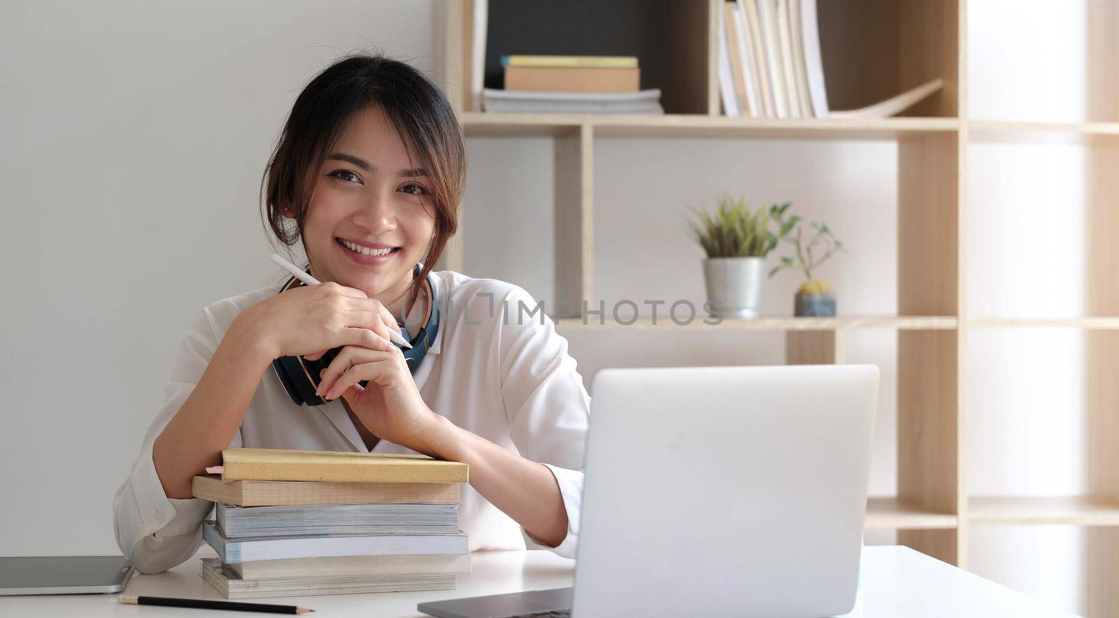 Smiling asian woman working  on the desk with books and laptop computer.