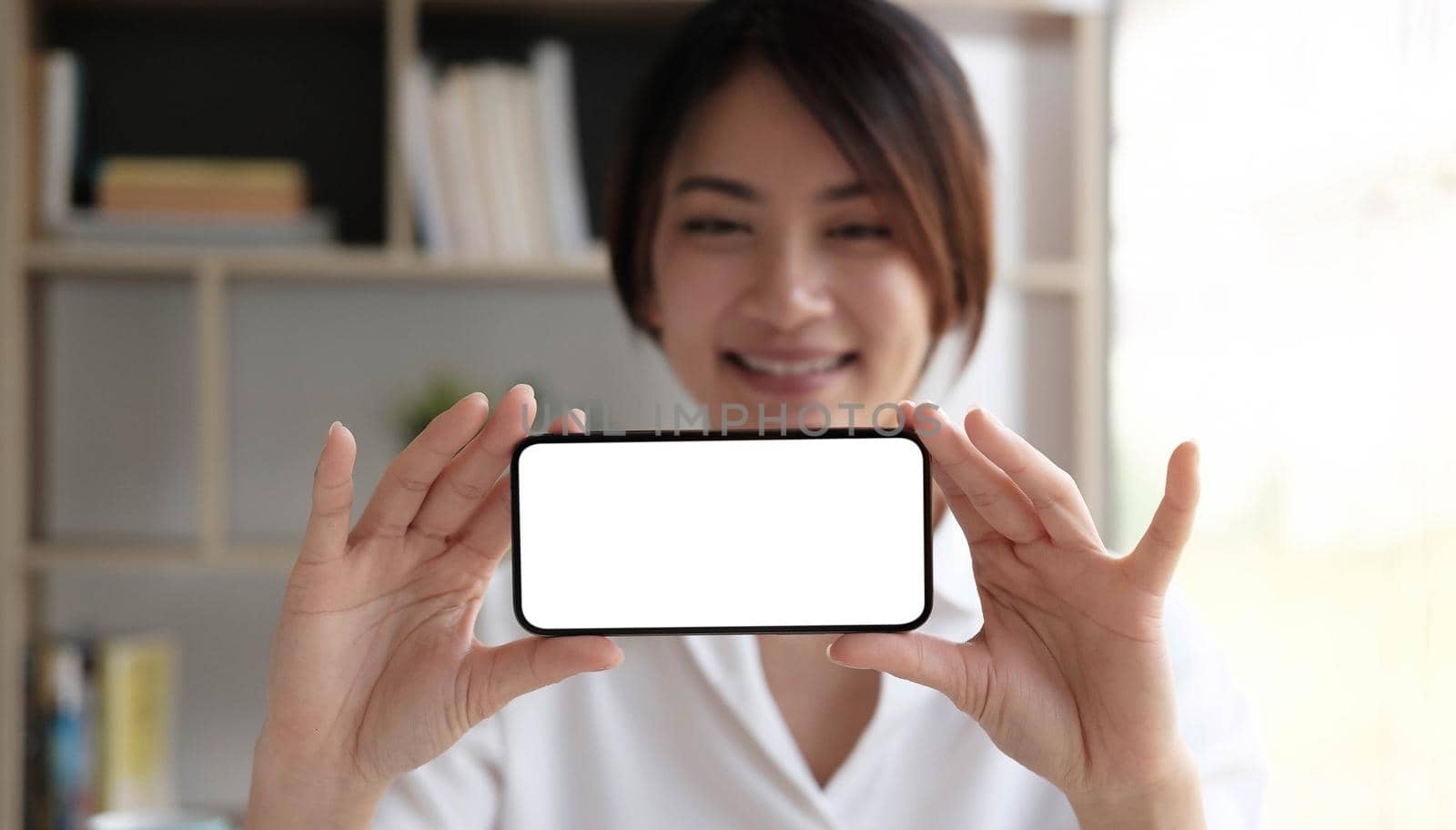 Cheerful young girl holding smartphone on hand with a blank screen. by wichayada