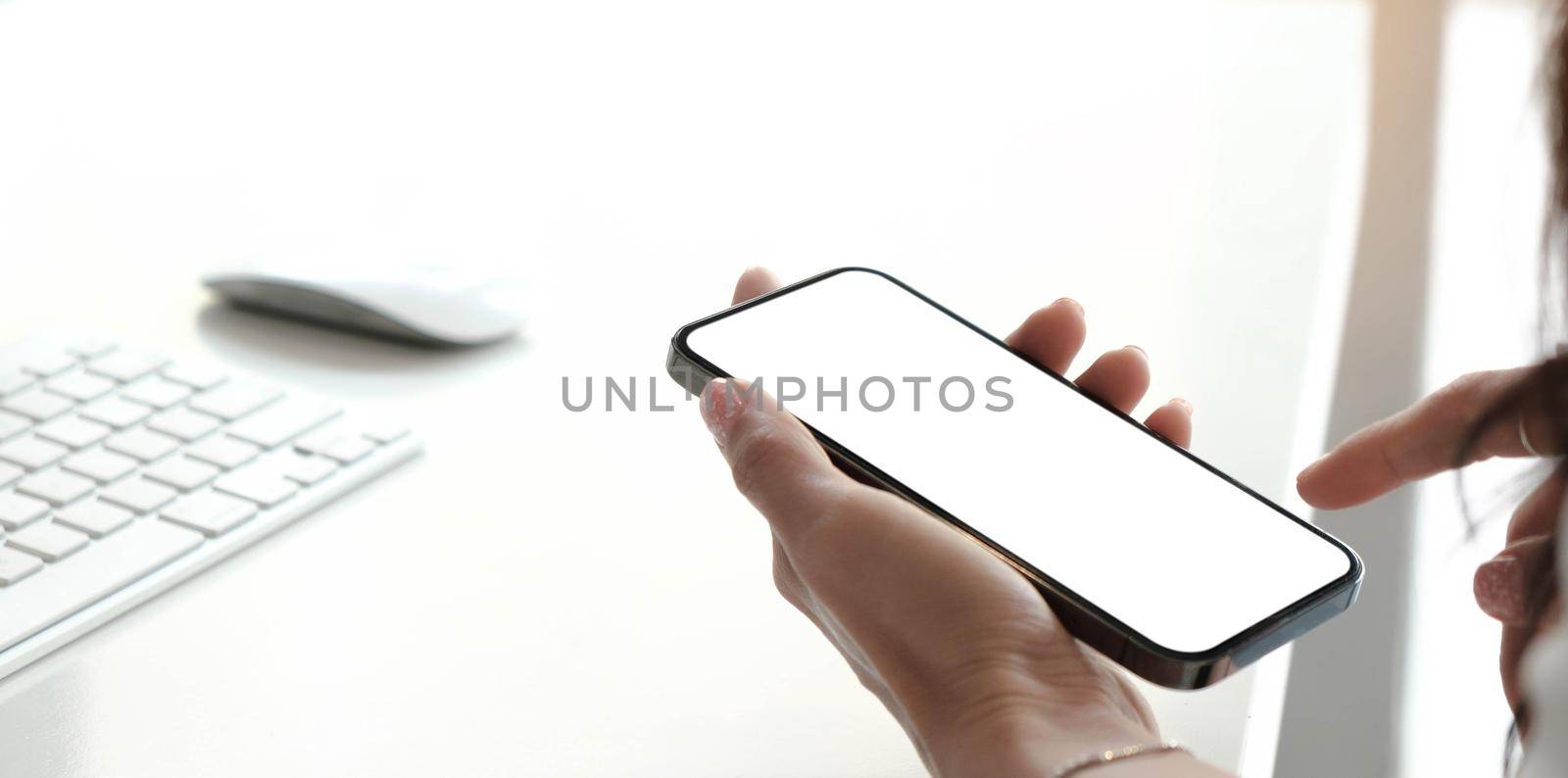 Mockup image blank white screen cell phone.women hand holding texting using mobile on desk at home office.  by wichayada